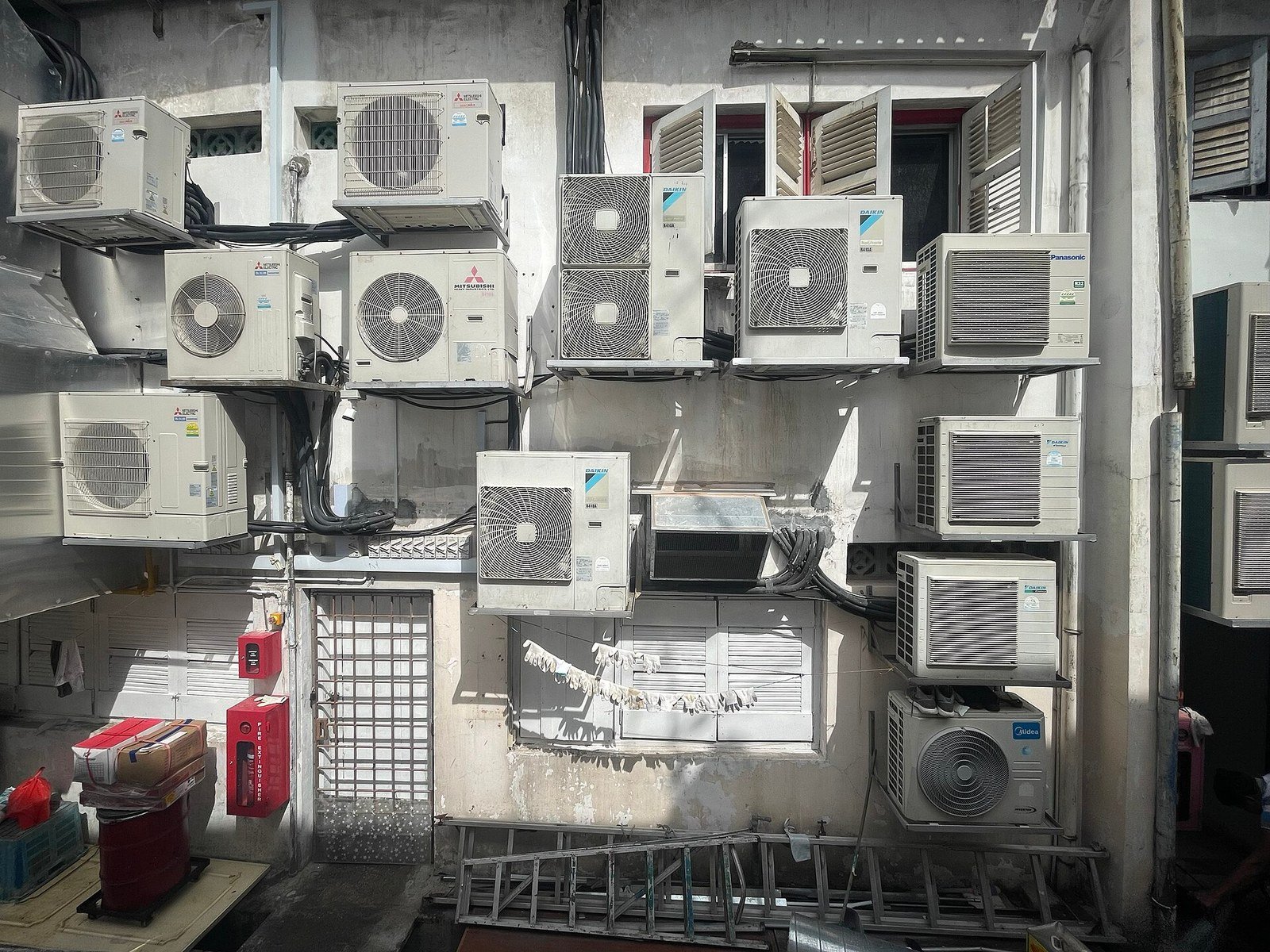 Multiple air conditioner external condenser units of various brands mounted on an outdoor wall of a building in Singapore